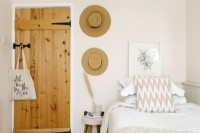 Pink feminine bedroom with framed art and sun hats on the wall. 