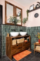 Twin round white sink bowls on a wooden unit in a green tiled bathroom