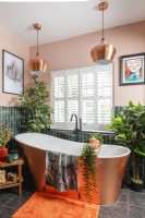 Free standing copper covered bathtub next to window with plantation shutters