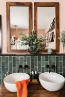 Twin round white sink bowls in a green tiled bathroom with orange painted walls and wood framed mirrors
