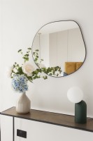 Mirror above a console table with vase of flowers and lamp
