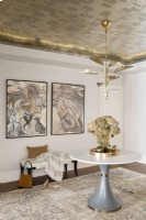 Room details with metal leaf wallpaper on ceiling decorated with pedestal table, bench and artwork.