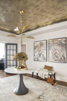 Modern foyer entrance decorated with pedestal table, artwork and gold metal leaf wallpaper on ceiling.