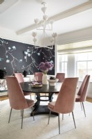 Dining room with round black dining table and pink high backed chairs.