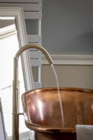 Modern swan's neck tap running into a large copper bath.
