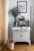 Vintage painted desk on landing, with old guidebooks, fishing rods and a large vase of blue Knapweed flowers