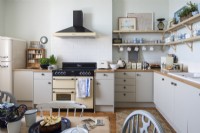 Simple contemporary kitchen with wooden shelving, beige coloured units an Aga cooker and a wooden worktop