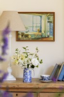 Vase of flowers on top of chest of drawers. Vintage painting of summer scene, and old books.