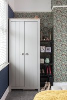 Wardrobe and shelves in bedroom with patterned wallpaper
