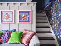 Oceanic artwork on white panelled wall above colourful cushions and next to a small white staircase