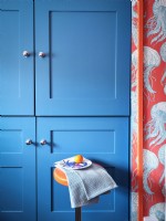 Modern blue kitchen units with sea inspired wallpaper and an orange stool