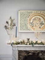 Mantelpiece decorated with fairy lights, house plants and candles below wall art