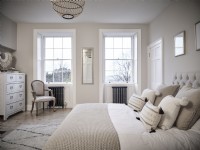 Neutral bedroom with a bed, upholstered chair, drawers and symmetrical windows