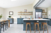 Modern classic kitchen with blue cupboards, island, open shelves, wooden bar stools, concrete floor tiles.