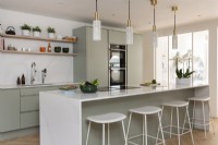 Contemporary light green kitchen with white marble island and brass light pendants.