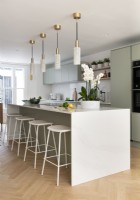 Modern contemporary kitchen with white marble island, light green units and brass light pendants.