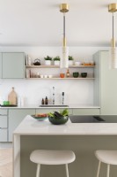Modern kitchen with light green cupboards, open shelves, brass light pendants and while island.