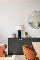 Modern dark grey sideboard with orange side table, black ceramic table lamp and round mirror.