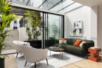 Modern extension conservatory with glass sliding doors, green fabric sofa, orange side table and cushions.