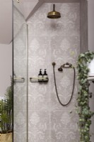 Detail of shower with pink patterned tiles and brass shower.