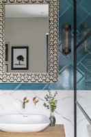 Detail of sink with marble and teal coloured tiles, brass taps and Moroccan inlay mirror 