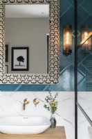 Detail of sink with marble and teal coloured tiles, brass taps and Moroccan inlay mirror 