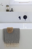 Detail of hamman towel over freestanding contemporary bath. Black taps.


