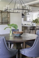 Round wooden dining table and upholstered chairs in open plan dining room and kitchen.