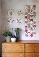 Colourful wall hanging on bare plaster wall above wooden sideboard