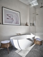 Neutral toned bathroom featuring white bath and wicker baskets