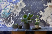 Detail of a dining table with plants and designer wallpaper .