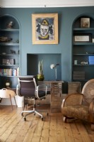 A designer vintage desk and chair against dark blue walls and built in shelving . 