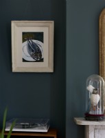 A painting of fish framed on a dark blue wall, next to a fireplace. 