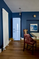 Detail of a dining room showing blue fridge and upright wall mounted radiator . 