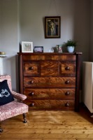 Antique chest of draws in a bedroom next to an antique chair covered in William Morris design fabric . 