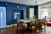 An open plan dining room , with a mid century table and chairs , infant of dark blue walls. 