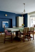 Dining room with dark blue painted walls, and vintage, antique table and chairs. 