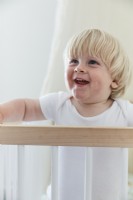 Smiling child baby boy in cot in nursery bedroom