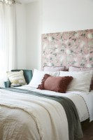 Double bed detail with fabric headboard with bird and floral patterns and throws, cushions, pillows and armchair