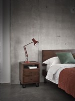 Orange bed against industrial concrete wall with side table and lamp