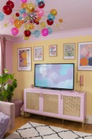 Corner of a colourful living room with pink sideboard and multicoloured glass chandelier
