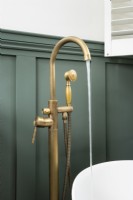 Floor standing brass bath taps against a green paneled wall in a country bathroom