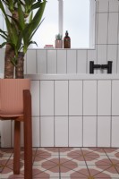 Bathroom detail with colourful vinyl flooring, black fittings, white tiles and a plant in a pink pot.
