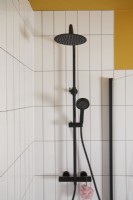 Bathroom detail with black shower fittings, white tiles and a yellow painted wall.