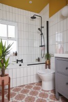 Bathroom with colourful vinyl flooring, black fittings, white tiles and yellow painted walls and ceiling.