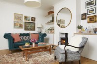 Living room with a teal blue sofa, armchair, wood-burning stove and vintage oil paintings on the wall.