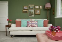 Living room with a cream sofa, vintage oil paintings and a green painted wall.