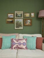 Living room detail with a cream sofa, vintage oil paintings and a green painted wall.