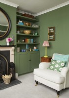 Living room with a cream armchair, fireplace, vintage oil paintings and green painted shelving.