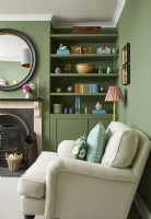 Living room with a cream armchair, fireplace, vintage oil paintings and green painted shelving.